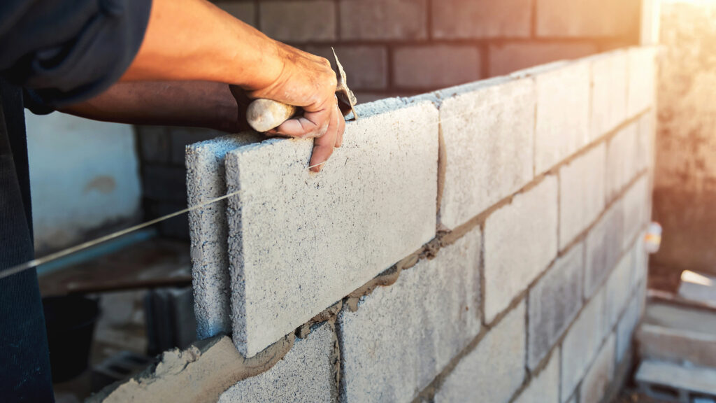 Maçon ajuste un parpaing sur un mur pour Ng Réno à Cuxac-Cabardès durant des travaux soignés,